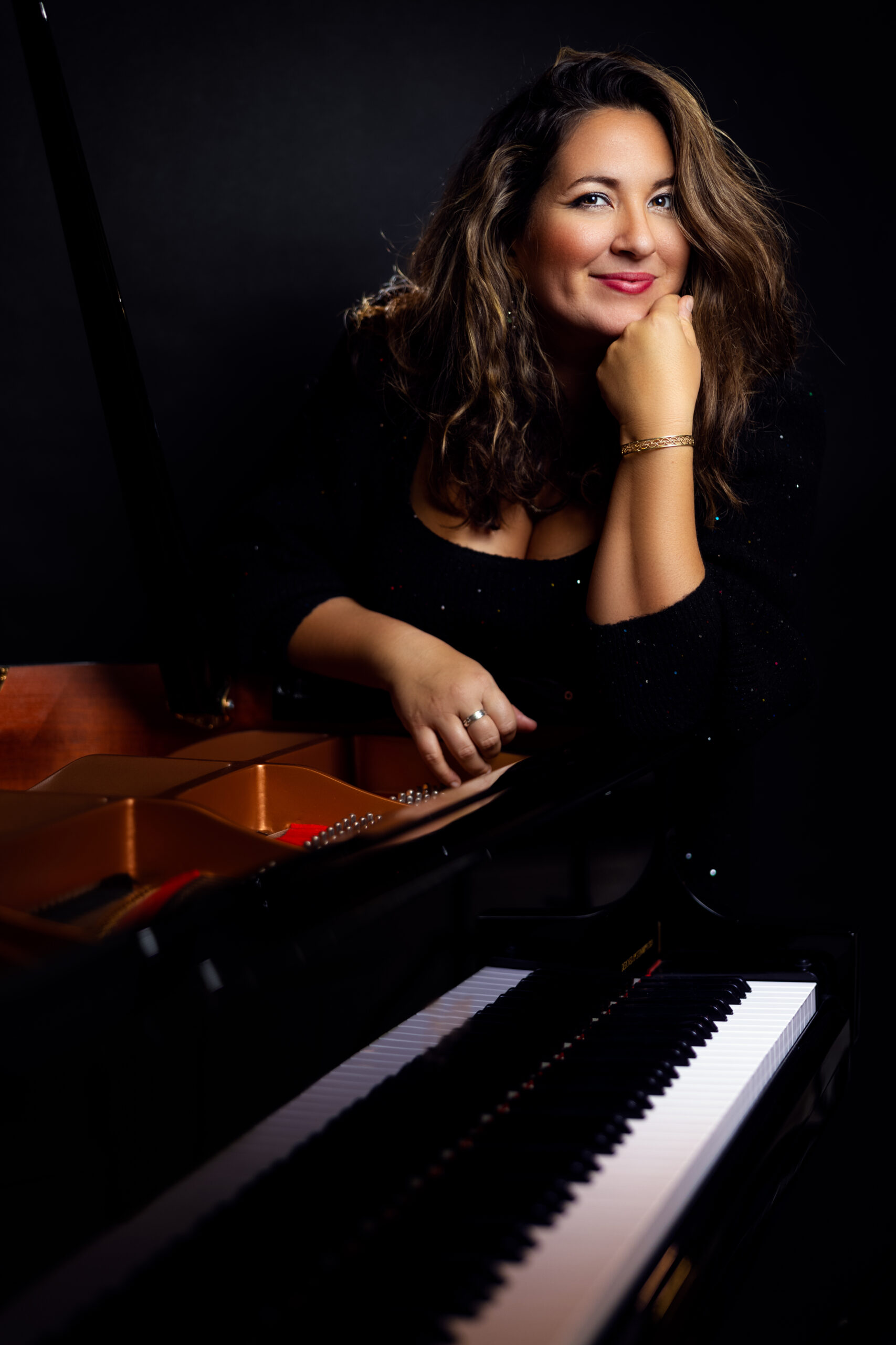 Nicole Zuraitis standing at the end of a piano dressed in black